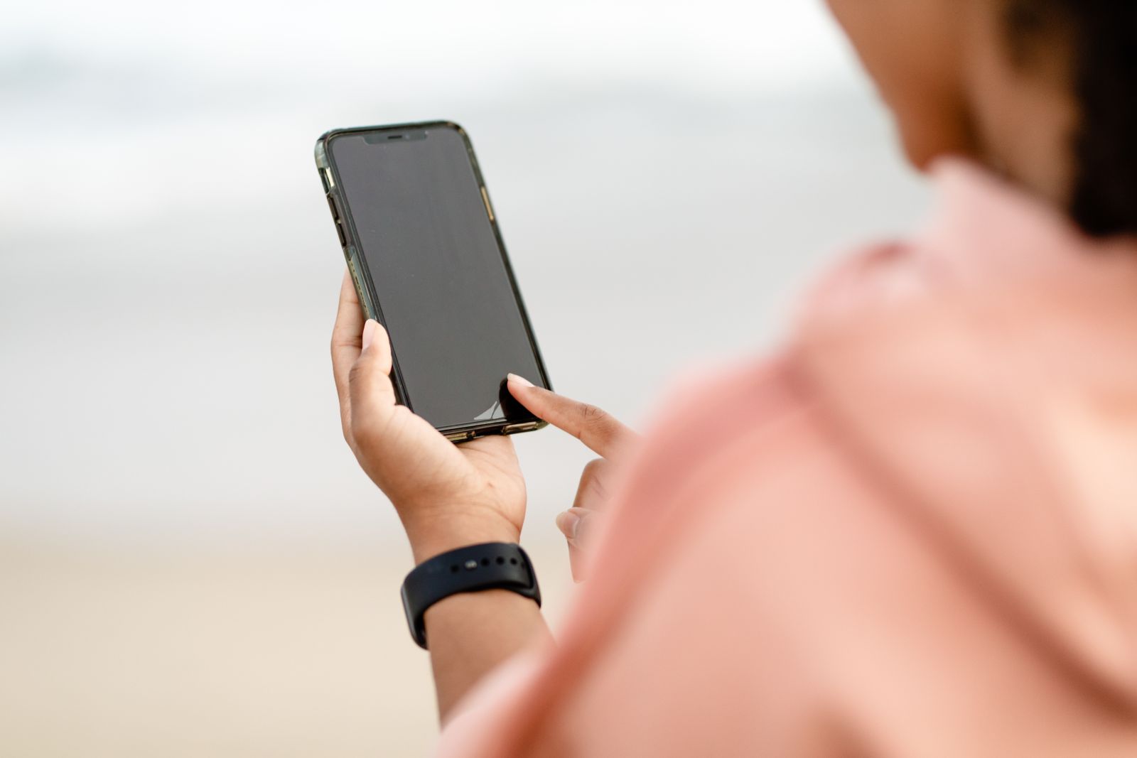 A hand using a smartphone outdoors.