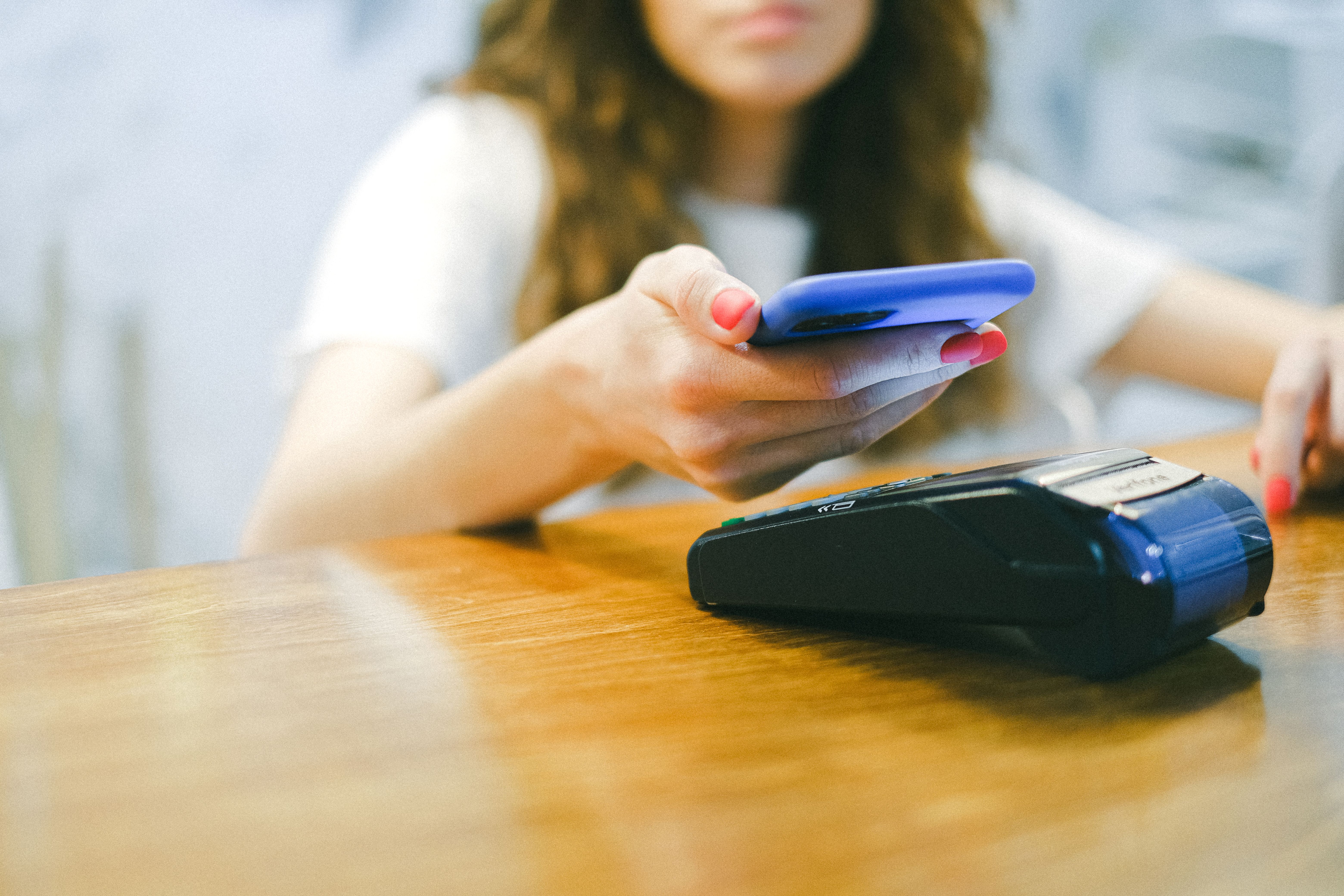 A customer completing a contactless mobile payment by holding a smartphone above a wireless payment terminal.