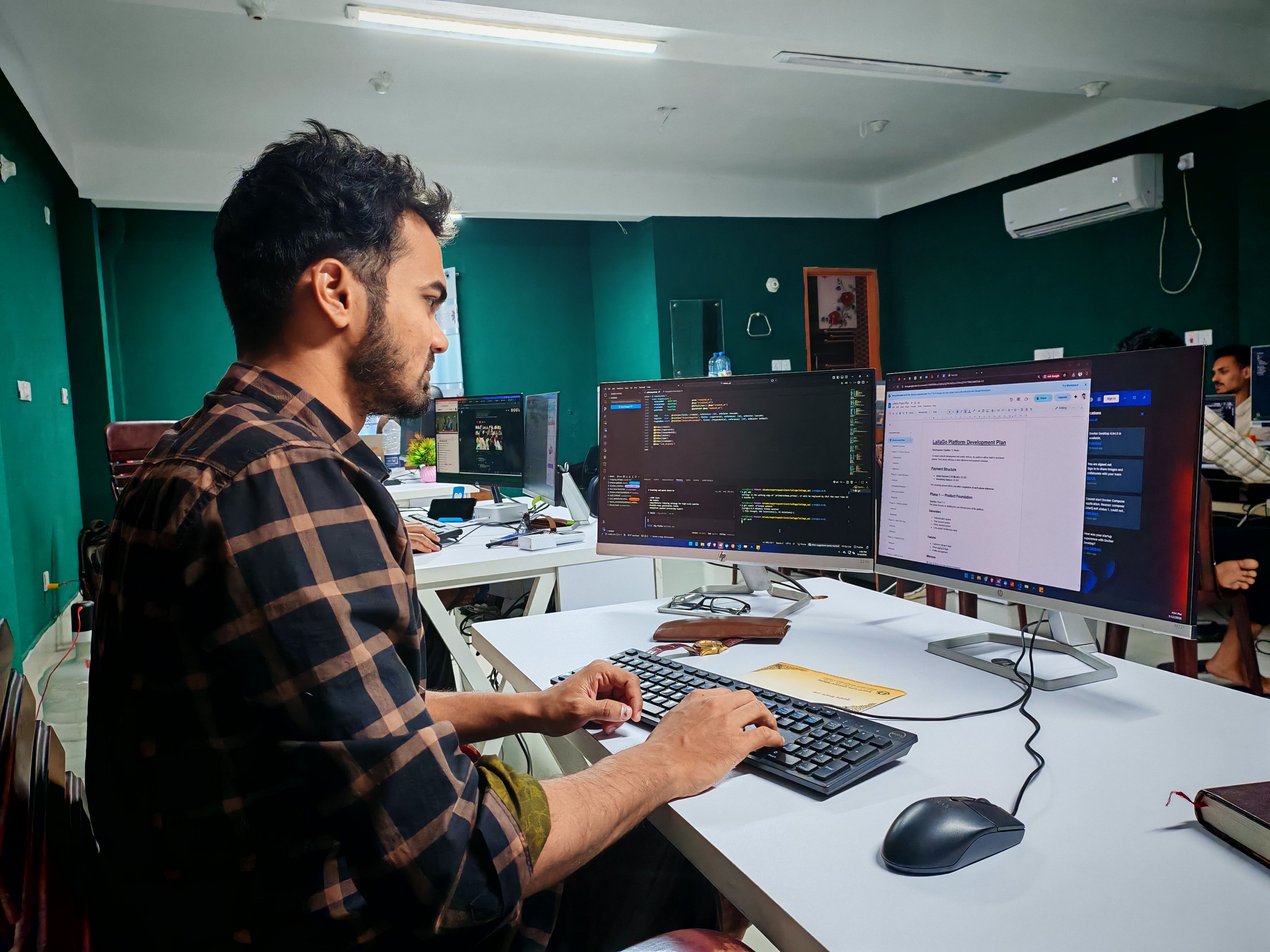 A software developer working on code and web applications across multiple desktop monitors in a modern office.