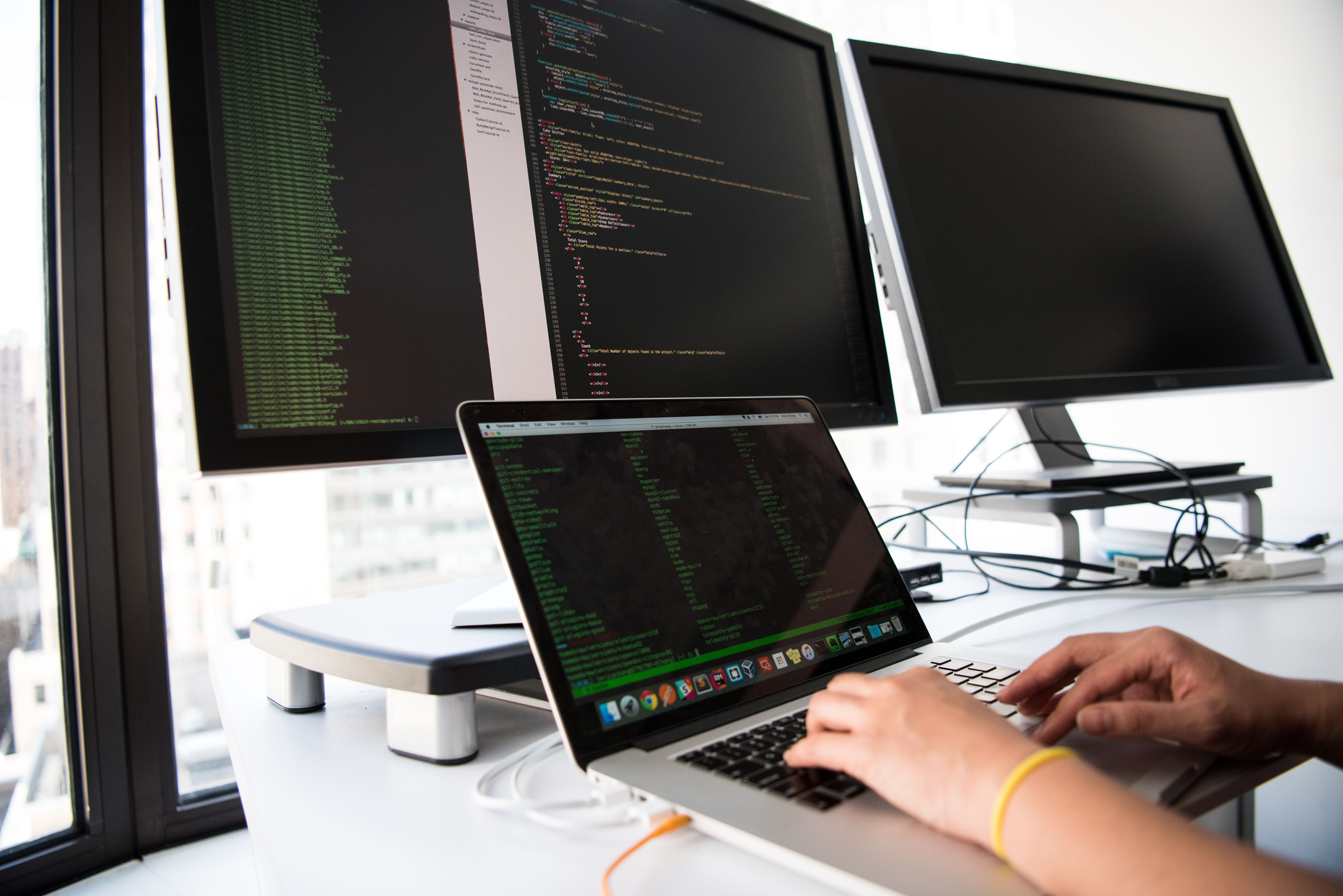 Developer typing on a laptop in front of multiple monitors.