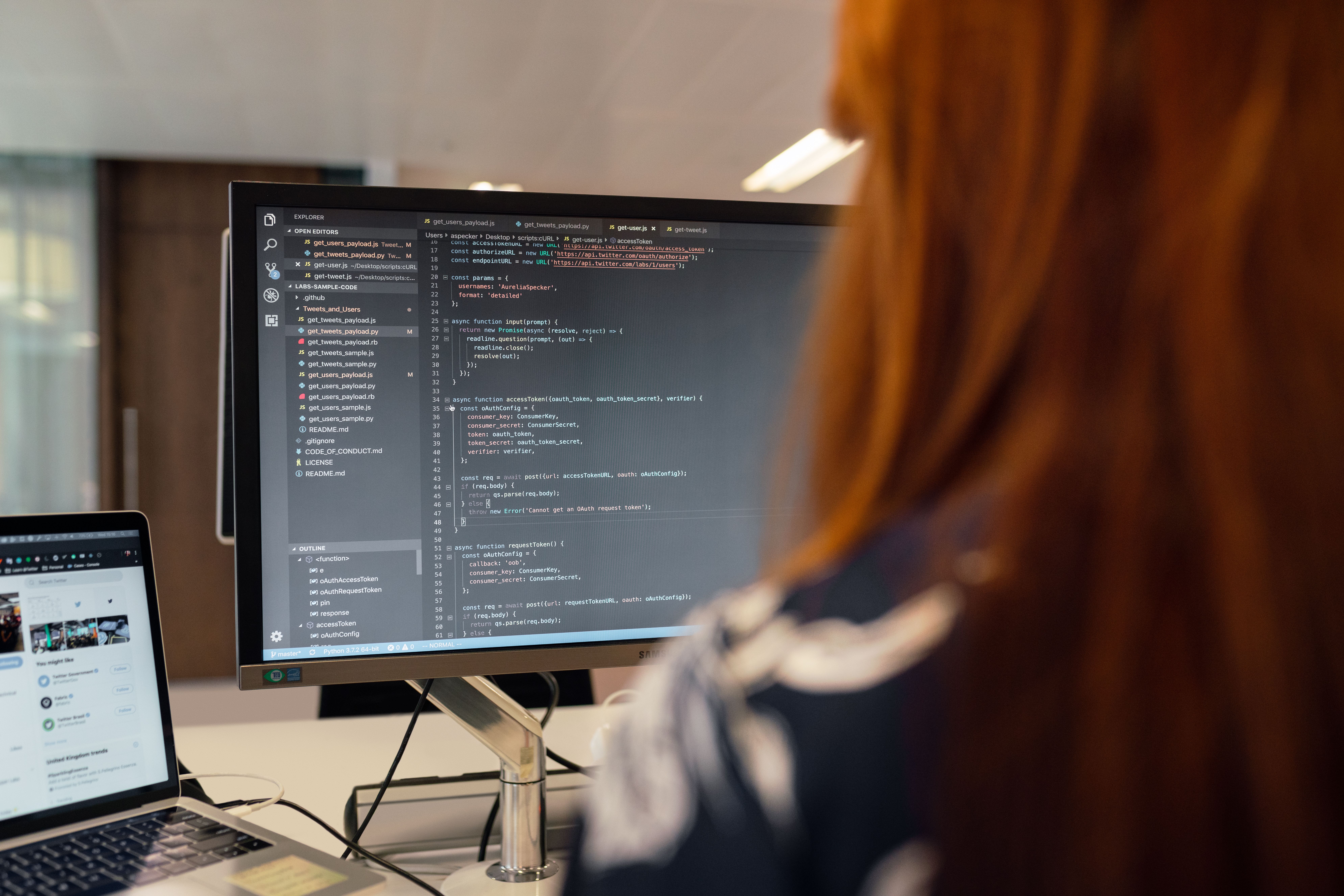 Software engineer analyzing code architectures and runtime system metrics across development monitors in a modern office.