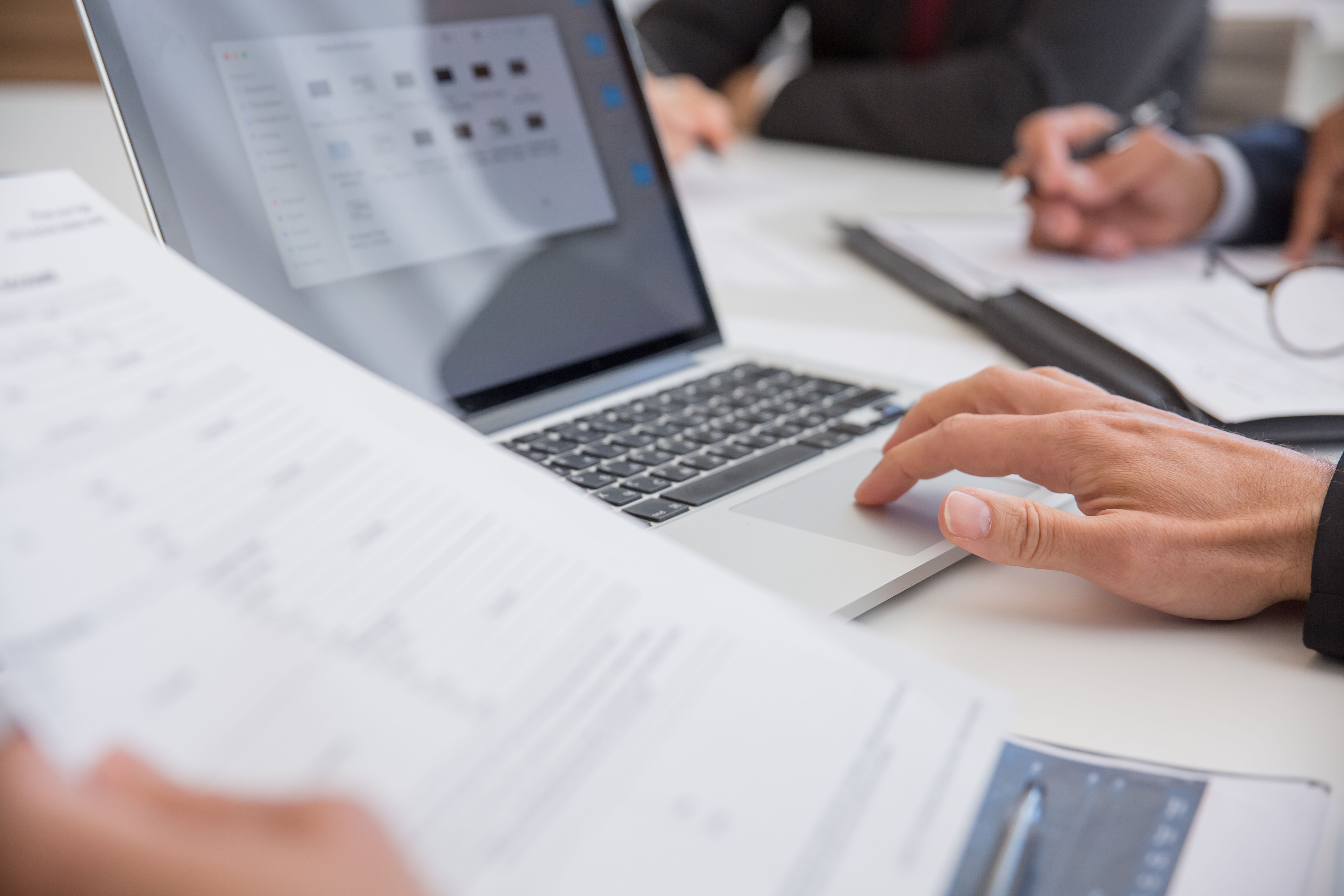 Hands reviewing documents and a laptop on an office desk.
