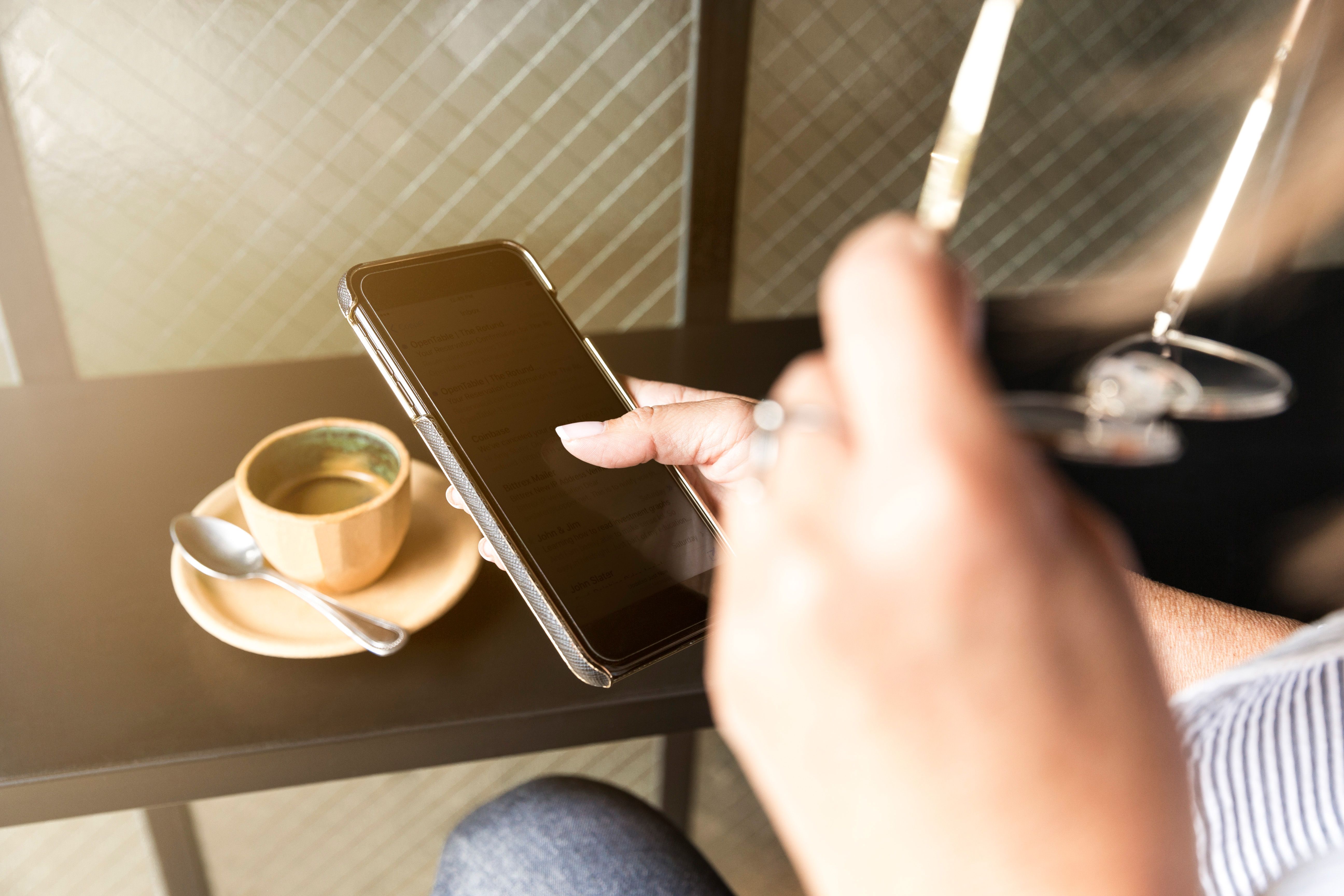 Photo illustration of a person checking a smartphone next to a cup of coffee on a table