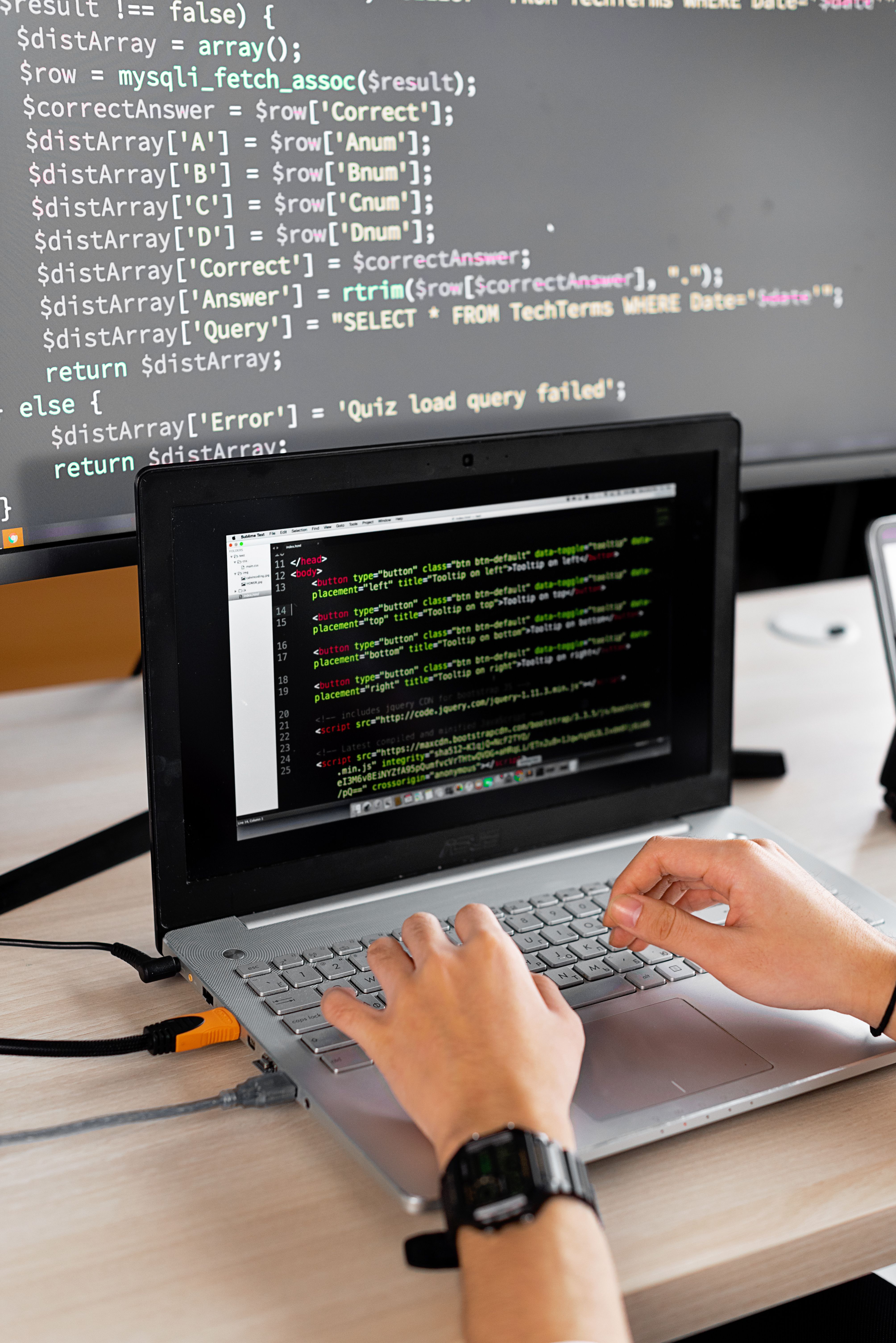 Photo illustration of a software developer coding at a laptop with a second monitor showing colorful code