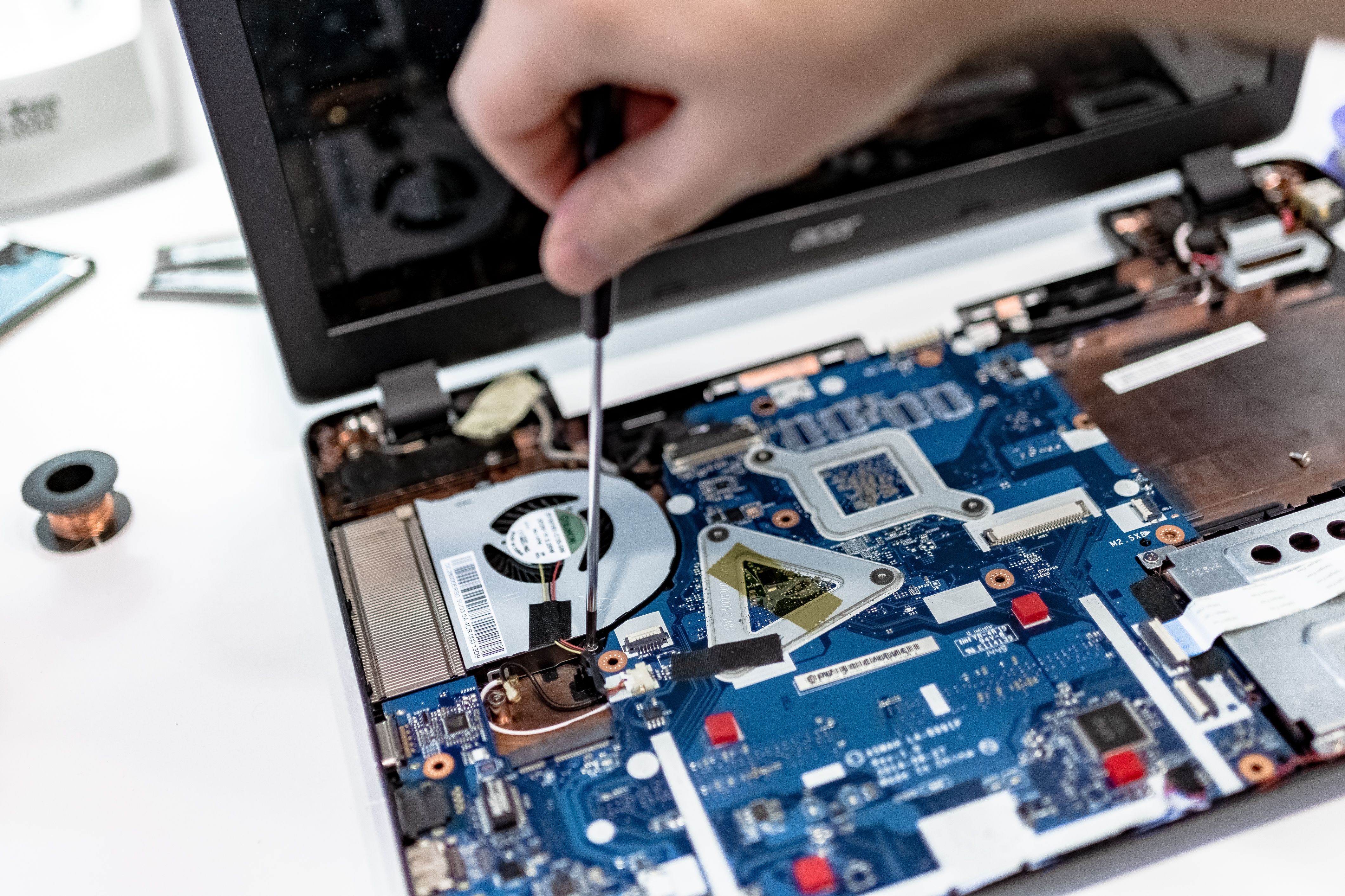 Close-up of a technician servicing a laptop motherboard with a precision screwdriver.