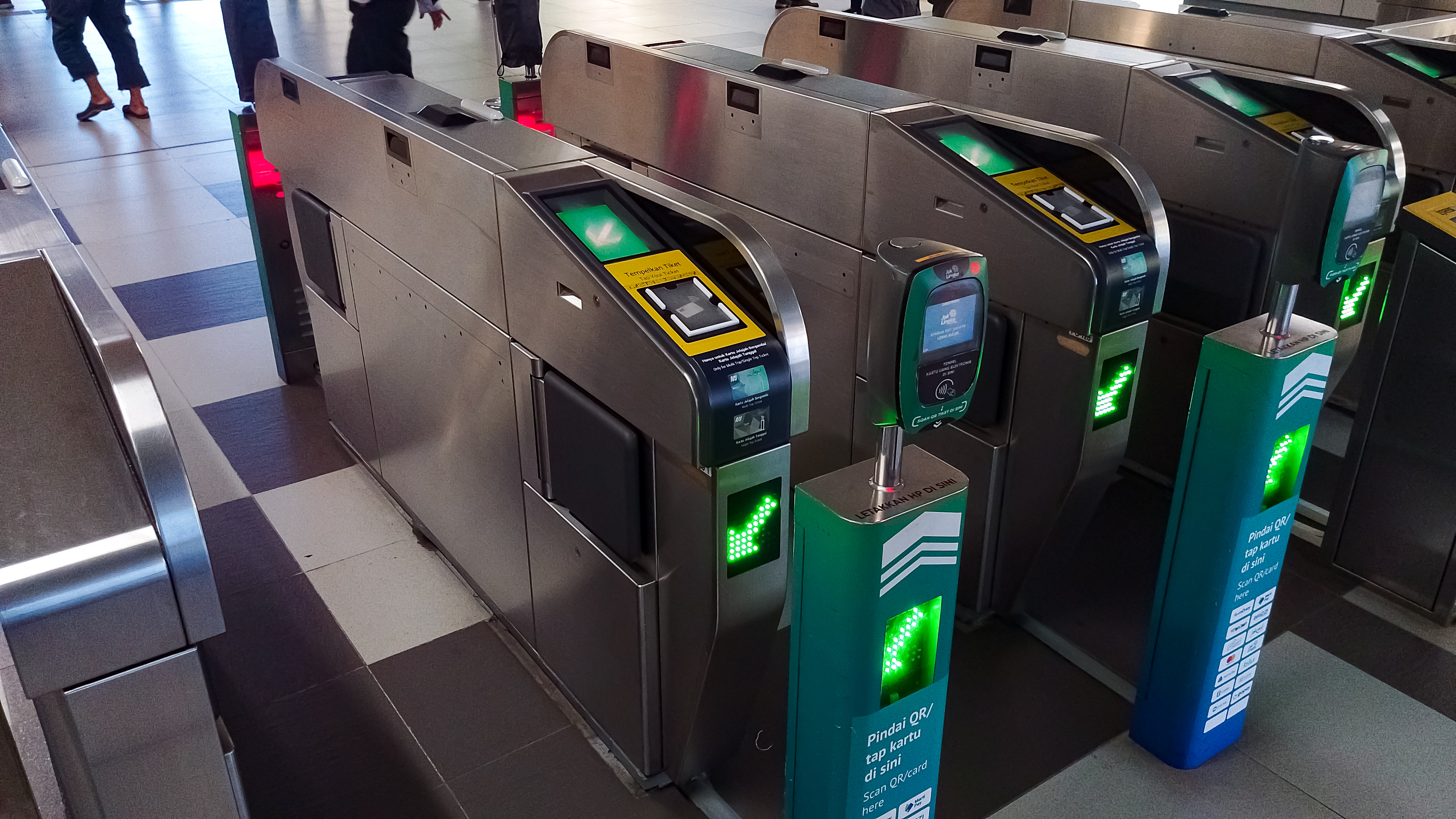 Ticket gates at Jakarta MRT station showing contactless smart card readers and optical QR code scanners.