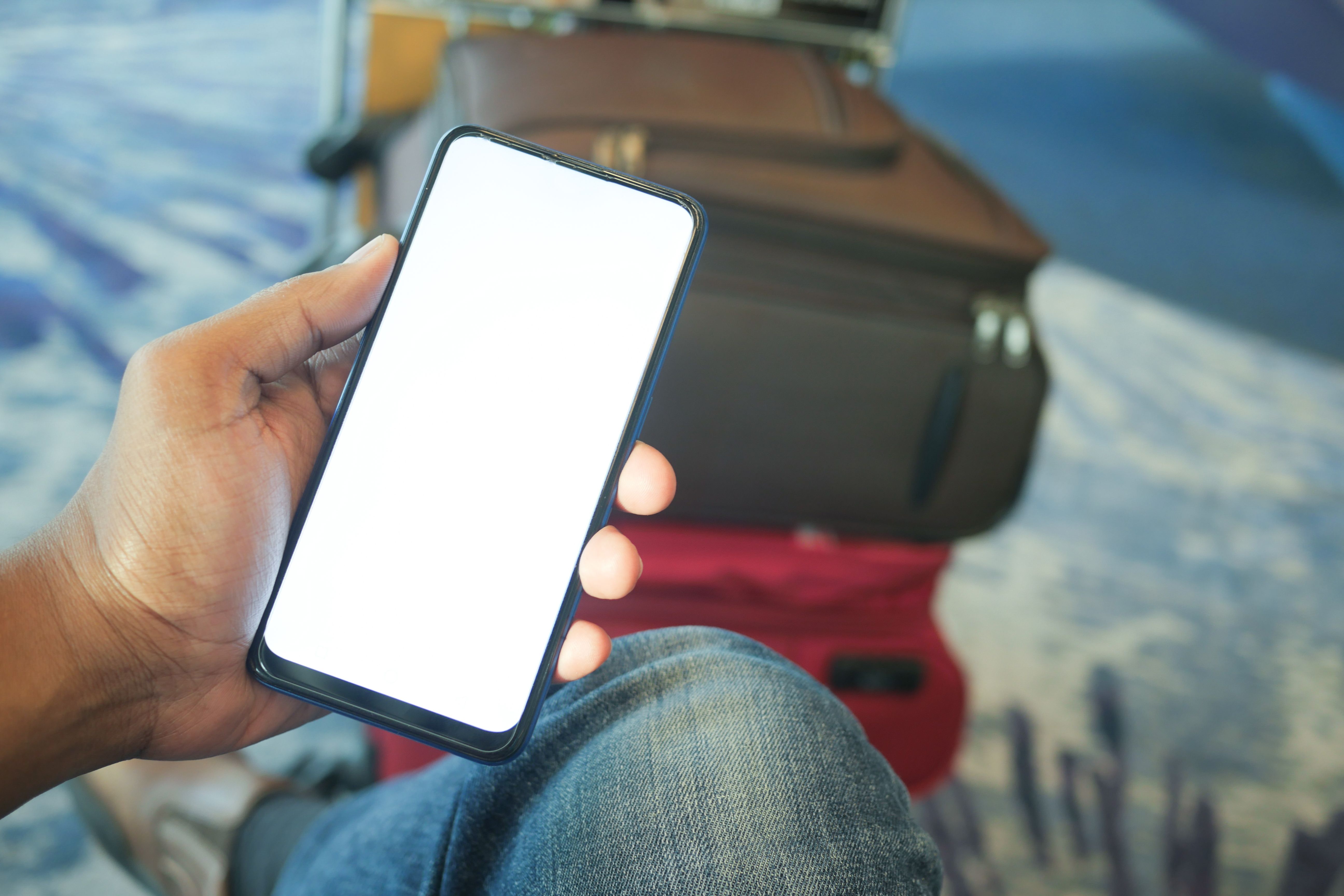 Close-up of a traveler holding a smartphone inside an airport terminal with luggage.