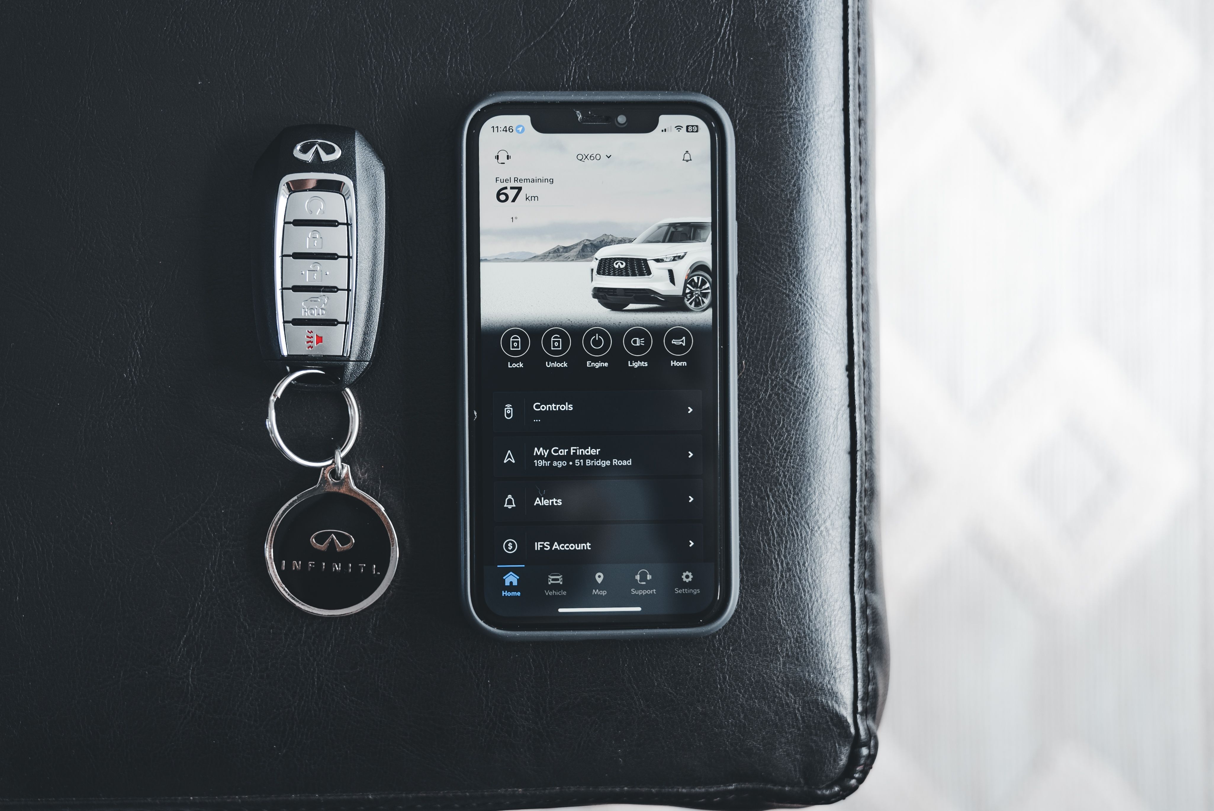 Close-up of a modern vehicle key fob and smartphone resting on a dark leather surface.