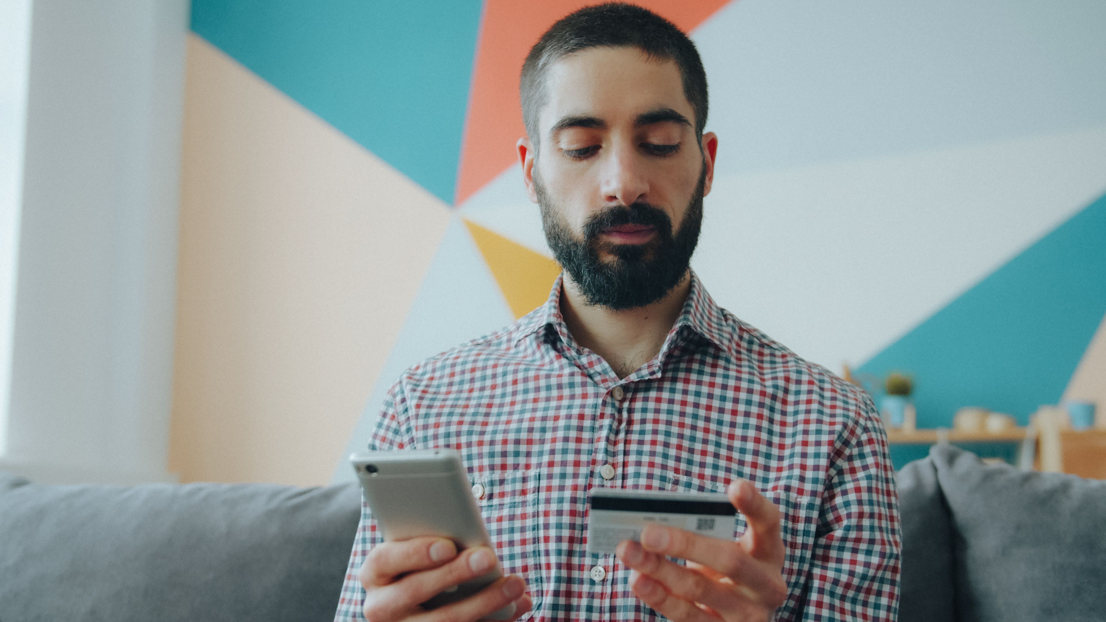 A man indoors using a smartphone and credit card for digital transactions.