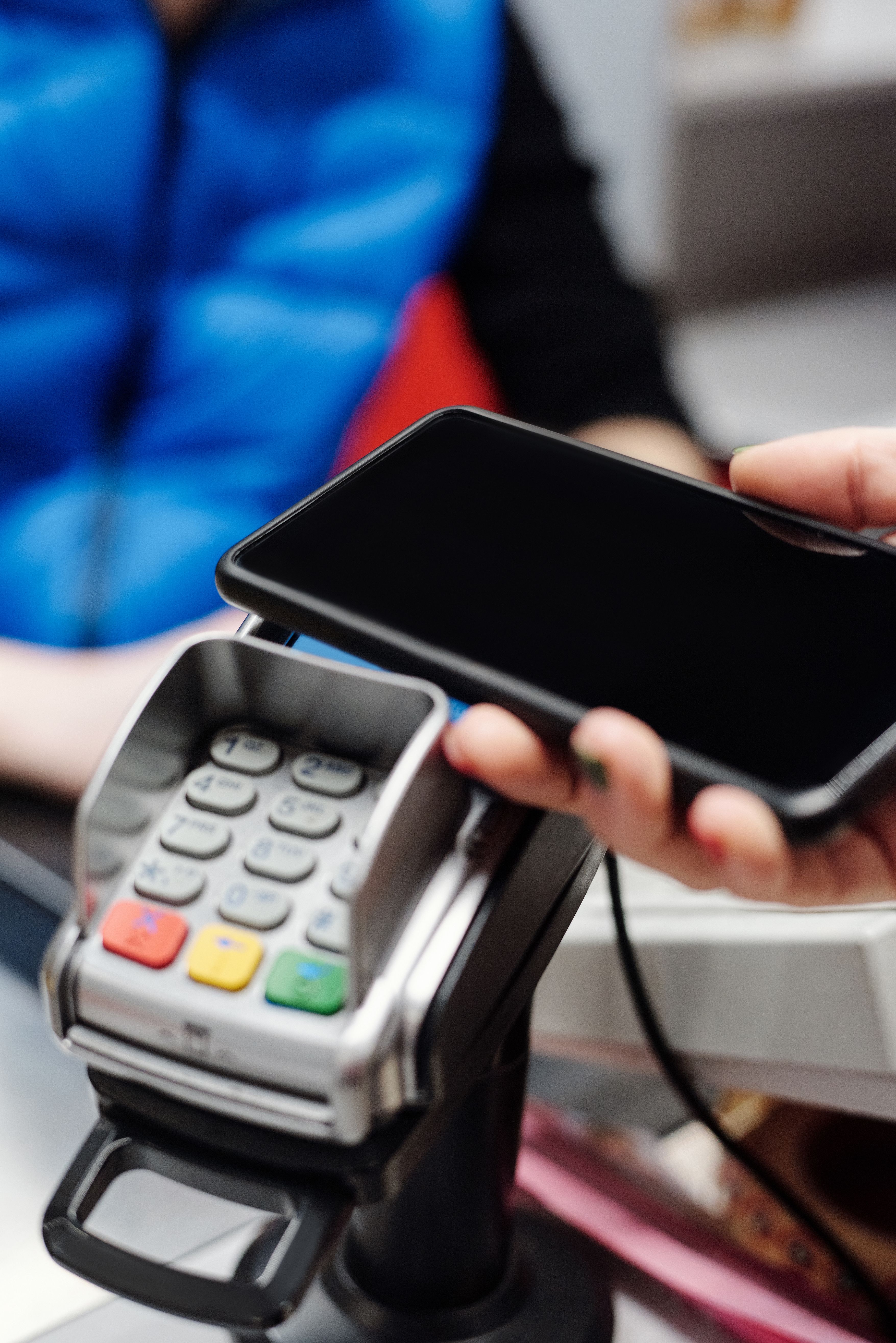 Close-up of a consumer making a contactless mobile payment by holding a smartphone above an electronic payment terminal.