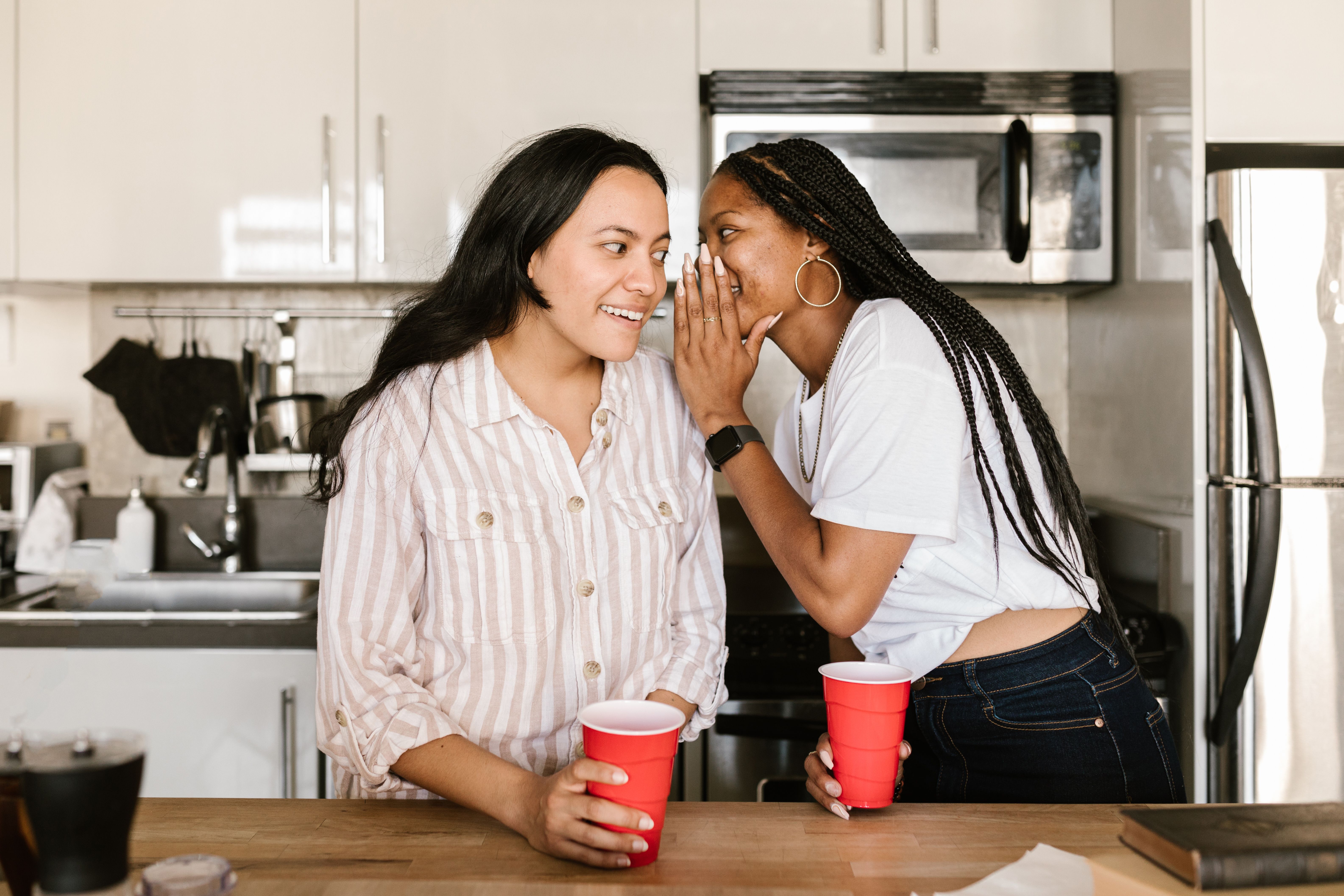 Two young women having an intimate private conversation indoors, whispering secrets in a modern room.