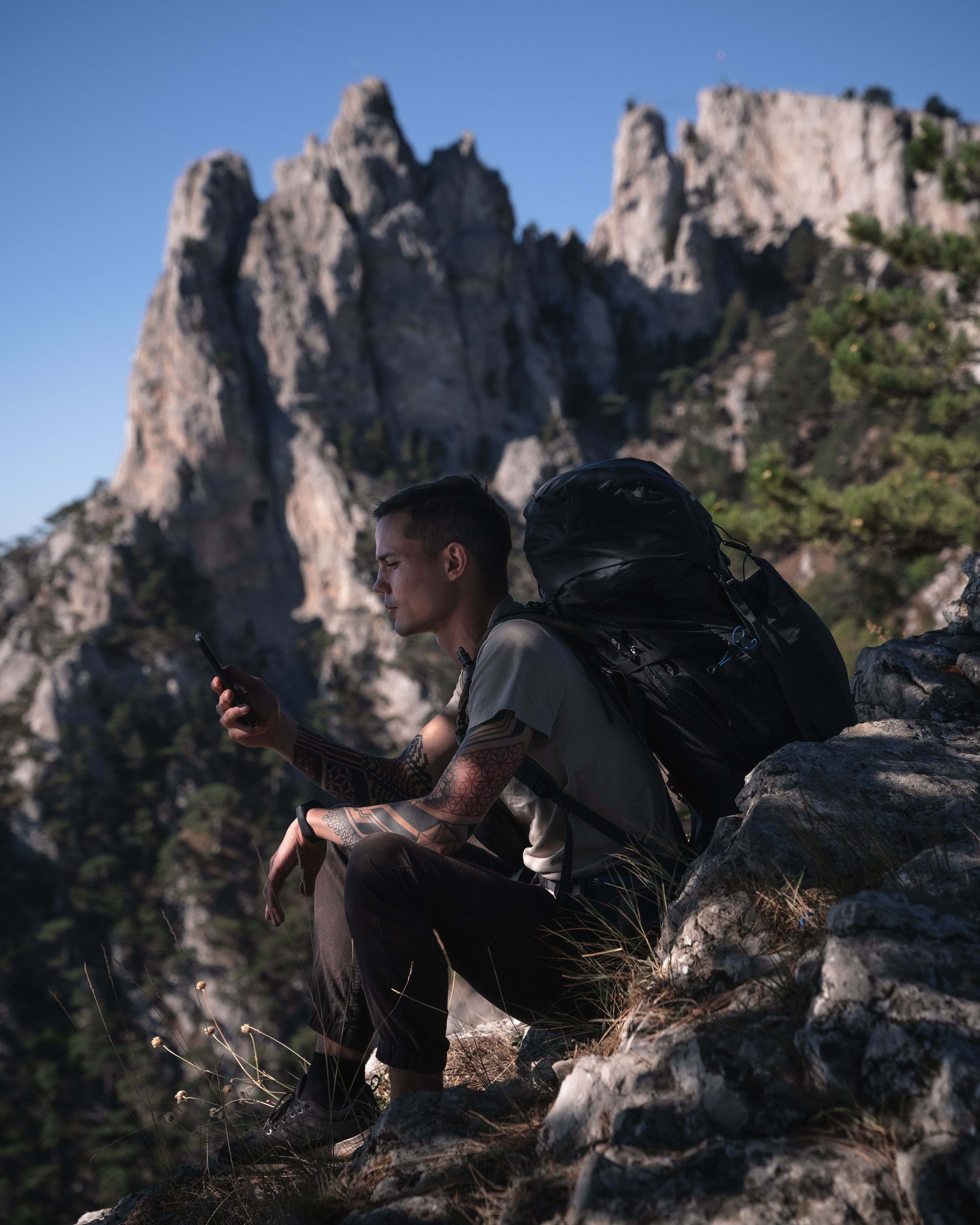 A hiker resting on a rocky mountain slope and checking a smartphone in a remote alpine landscape.