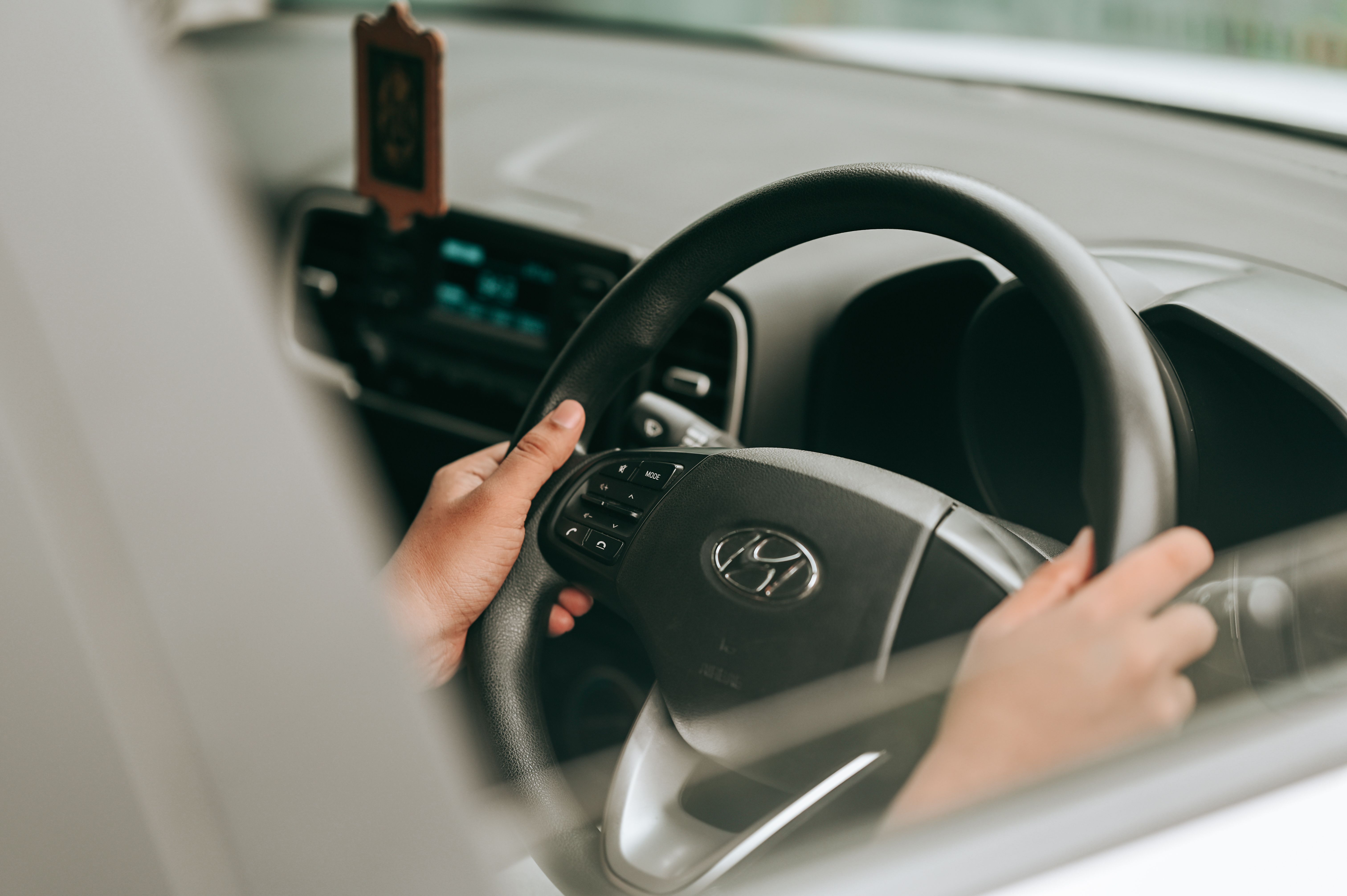 A driver holding the steering wheel with hands firmly placed inside a car.