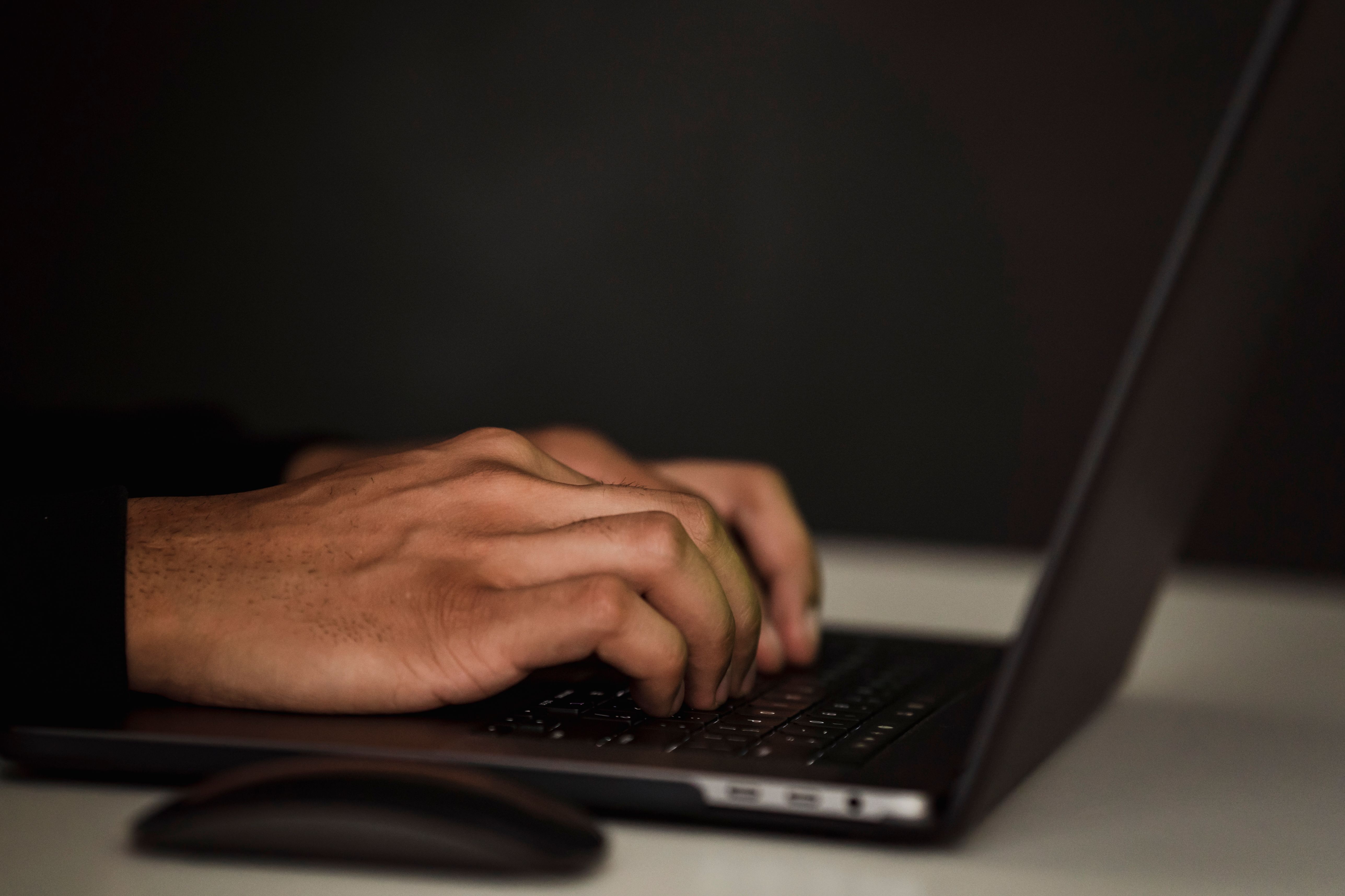 Close-up of a person typing on a laptop keyboard in a dimly lit workspace, entering text into an online form.