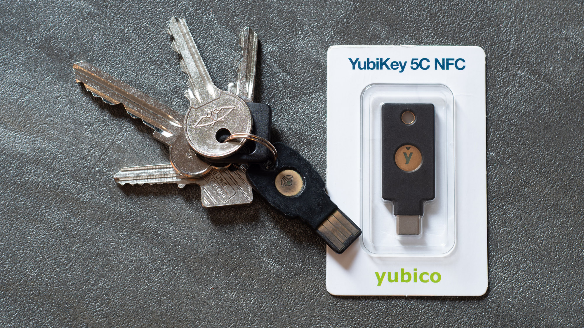 Foto jarak dekat kunci keamanan perangkat keras YubiKey 5C NFC berdampingan dengan anak kunci fisik.